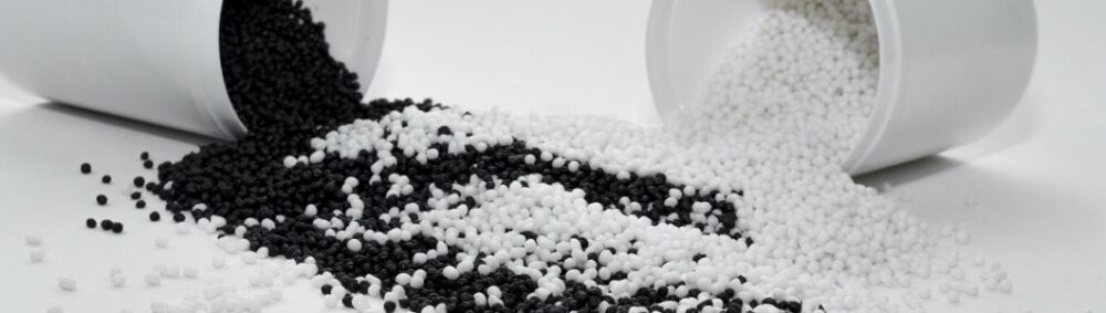 Two containers tipped over, spilling black and white plastic pellets onto a flat surface, with the pellets mixing in the center.