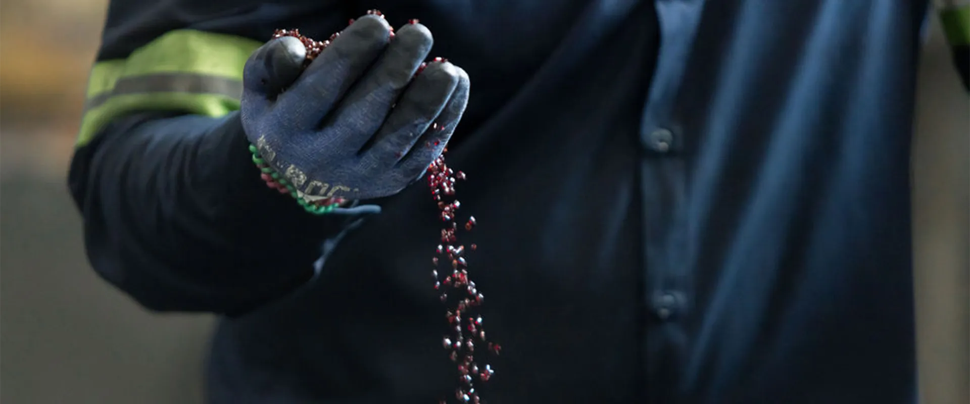 A person wearing a dark uniform and gloves holds and lets red plastic pellets fall from their hand.