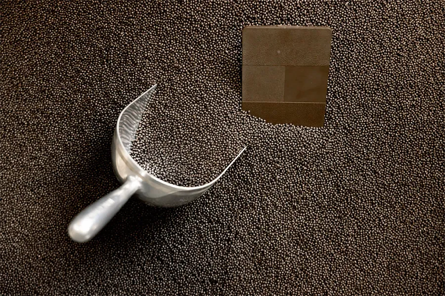 A metal scoop rests on a large pile of small brown pellets, with a square patch of smooth surface exposed in the pile.