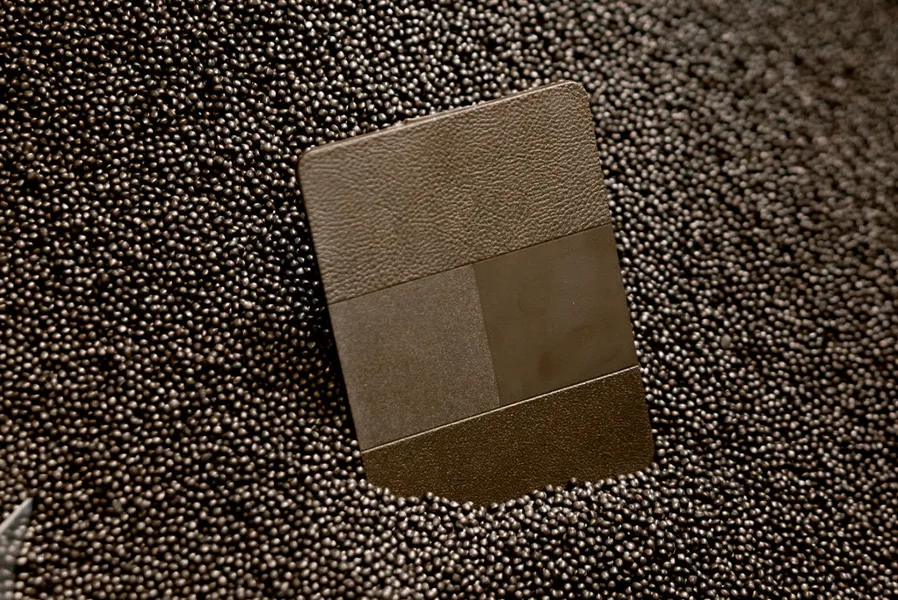 A rectangular chip with textured and smooth sections is partially embedded in a surface covered with small, round metallic beads.