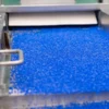 Close-up of blue plastic pellets on a conveyor belt in an industrial setting.