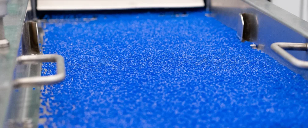 A close-up view of blue plastic pellets being processed on an industrial conveyor.