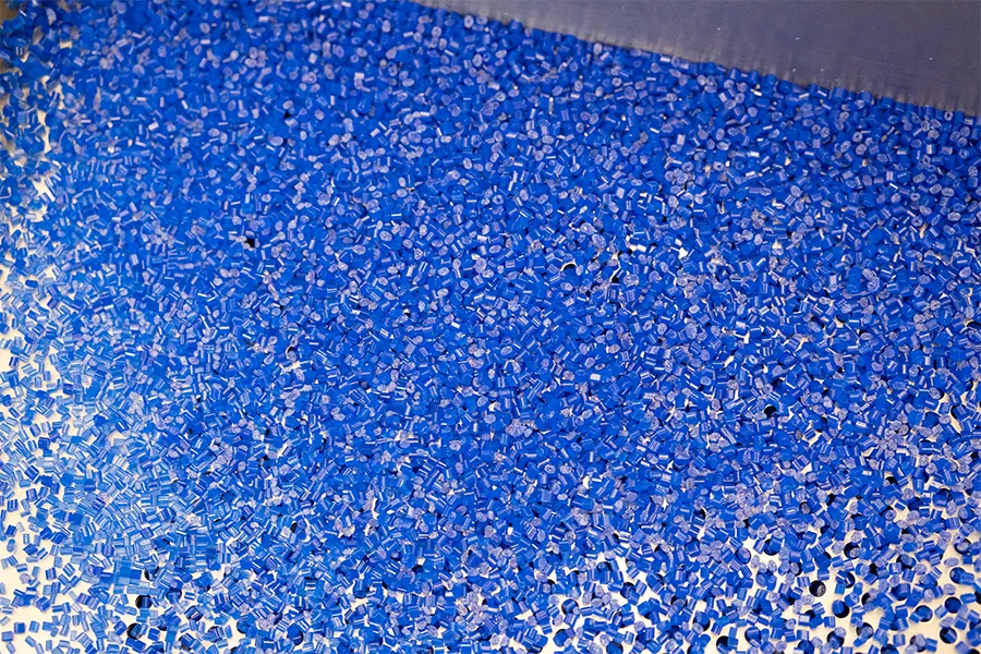 A large quantity of small blue plastic pellets is spread across a flat metallic surface.
