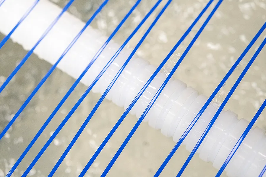Close-up of blue plastic strings stretched diagonally over a textured white cylindrical object, with a blurred, light-colored background.