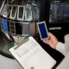 A person holds a rectangular blue sample in front of a machine, with a clipboard of printed data visible in the other hand.