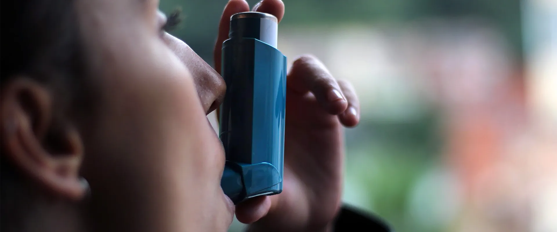 Close-up of a person using a blue asthma inhaler, with the inhaler held to their mouth.