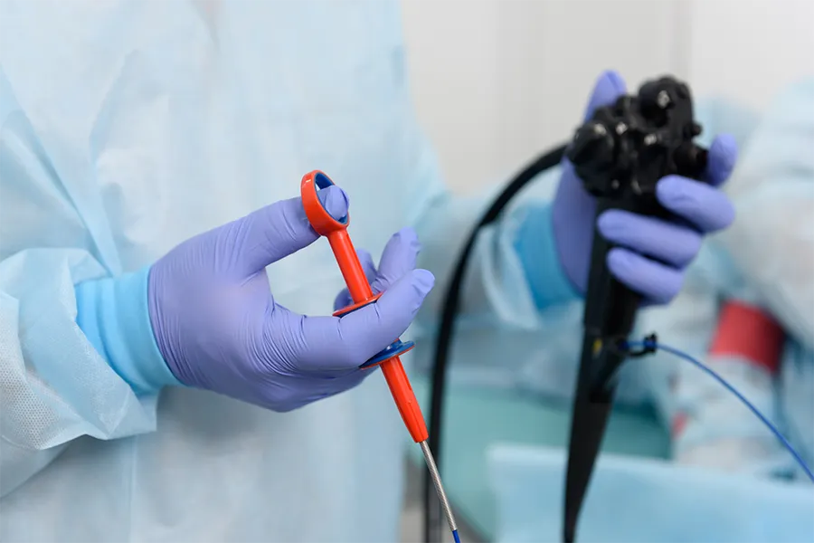 A medical professional wearing gloves holds an endoscope and a surgical tool, preparing for an endoscopic procedure.