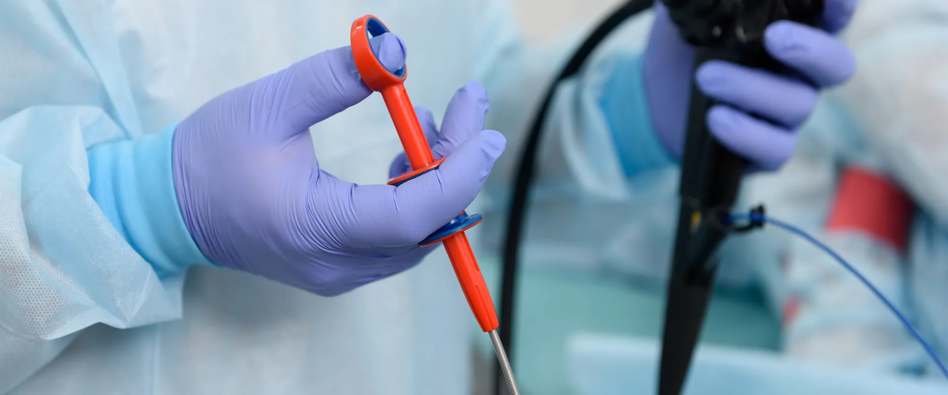 A person wearing surgical gloves and a medical gown holds an endoscopic instrument, preparing for a medical procedure.
