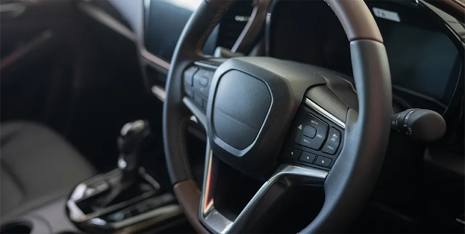 Close-up view of a modern car interior focusing on the steering wheel, dashboard controls, and gear shift.