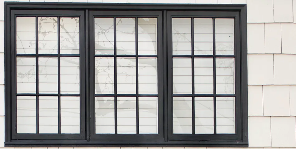A black-framed three-panel window with grid patterns is set in a white shingled wall.