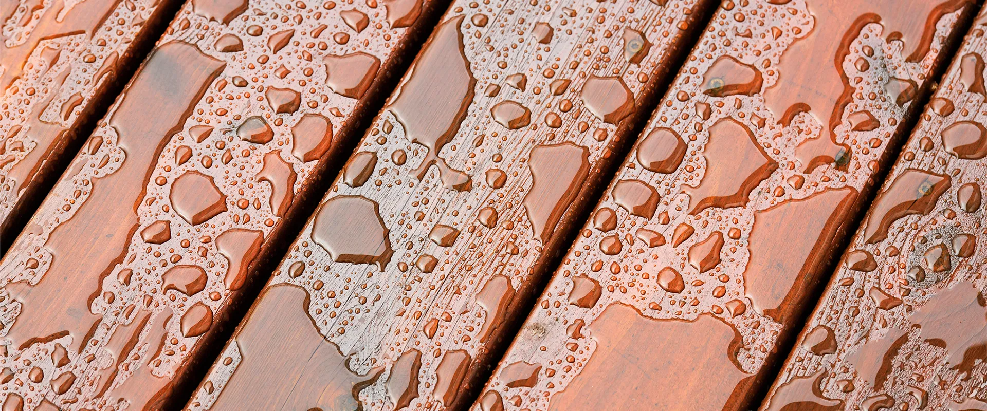 Close-up of water droplets scattered on wooden deck planks, showing wet and dry areas with natural wood grain visible.