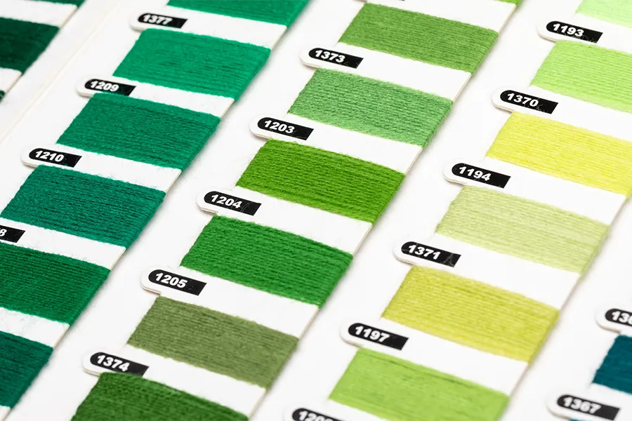 Close-up of labeled green and yellow-green fabric swatches arranged in rows on a white background, showing various shades and texture samples.