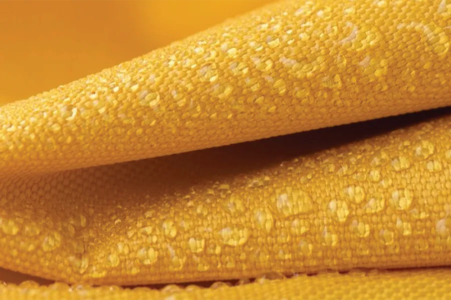 Close-up of yellow water-repellent fabric with visible textured surface and droplets beading on the material.