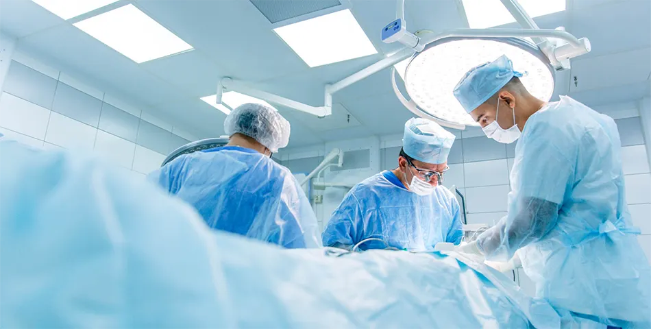 Three surgeons in scrubs and masks perform a surgical procedure under bright operating room lights in a sterile hospital environment.