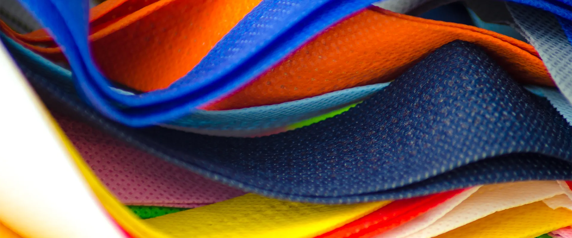 Close-up of layered, colorful textured fabric pieces stacked and overlapping, including shades of blue, orange, yellow, pink, and red.