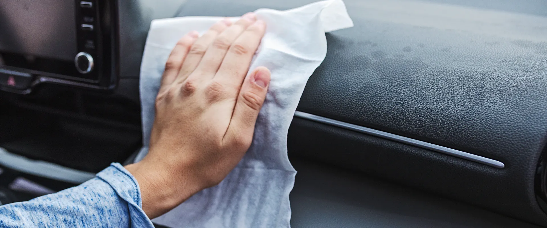 A person wipes the dashboard of a car with a white cleaning cloth or wipe.