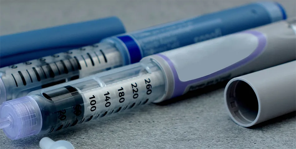 Close-up of insulin pens and their caps lying on a gray surface.