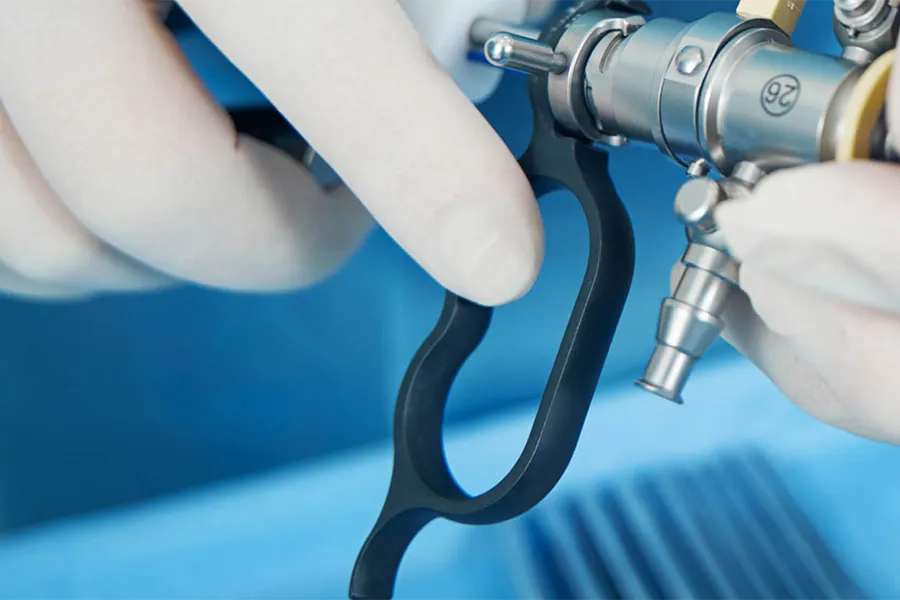 A close-up of gloved hands operating a piece of medical equipment, possibly an endoscope, against a blue background.