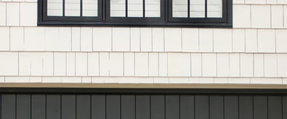 Close-up of a building exterior showing white vertical siding, a row of black-framed windows at the top, and black horizontal paneling at the bottom.