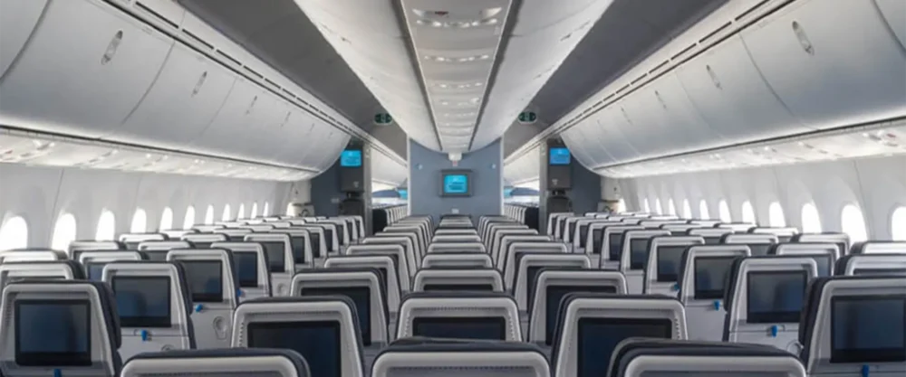 View of an empty airplane cabin showing rows of economy class seats with personal screens and overhead compartments.