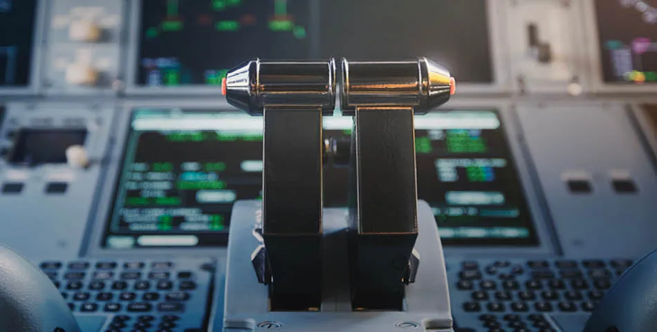 Close-up view of aircraft throttle levers in the cockpit, with illuminated flight control panels and digital displays in the background.