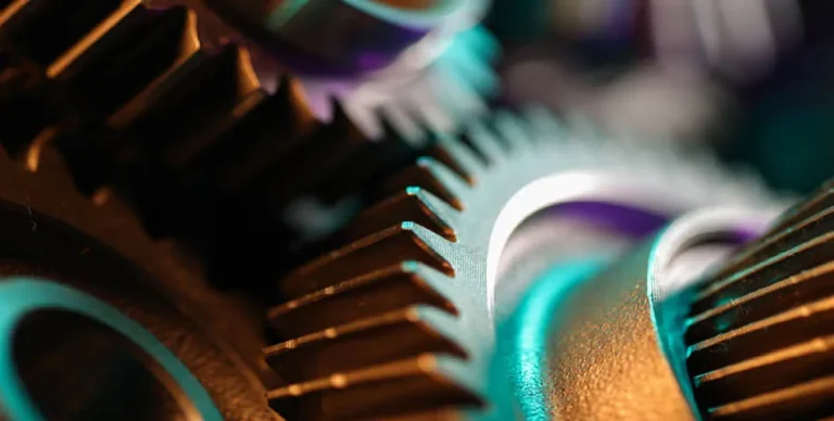 Close-up view of interlocking metal gears, showing detailed teeth and edges with a mix of warm and cool lighting.