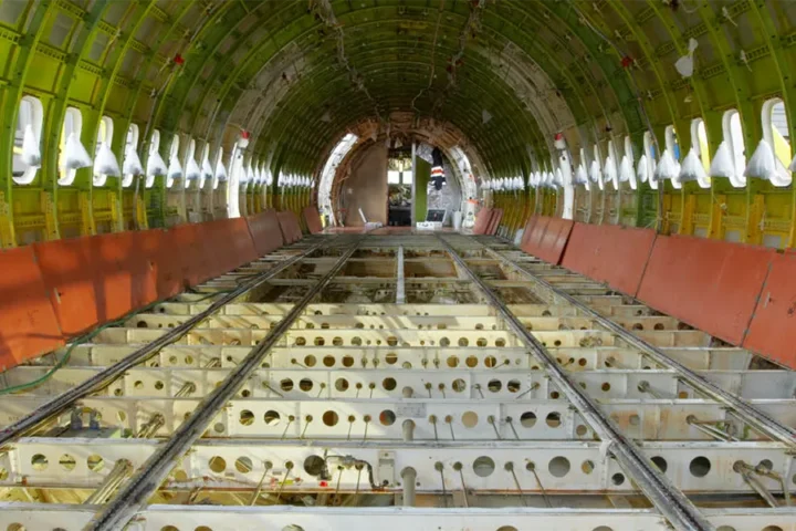 Interior view of an empty airplane fuselage showing exposed metal framework, with no seats or flooring installed.