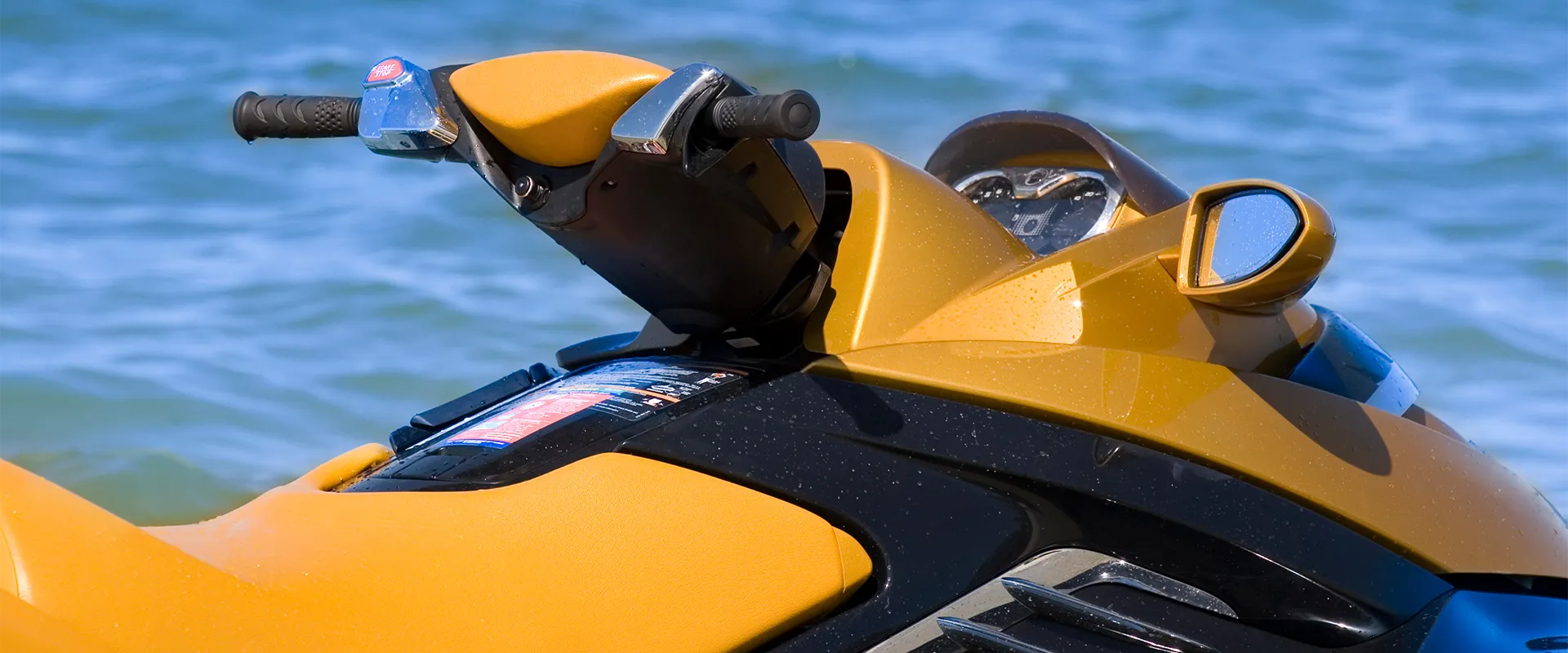 Close-up view of the handlebars and dashboard of a yellow personal watercraft, with blue water in the background.