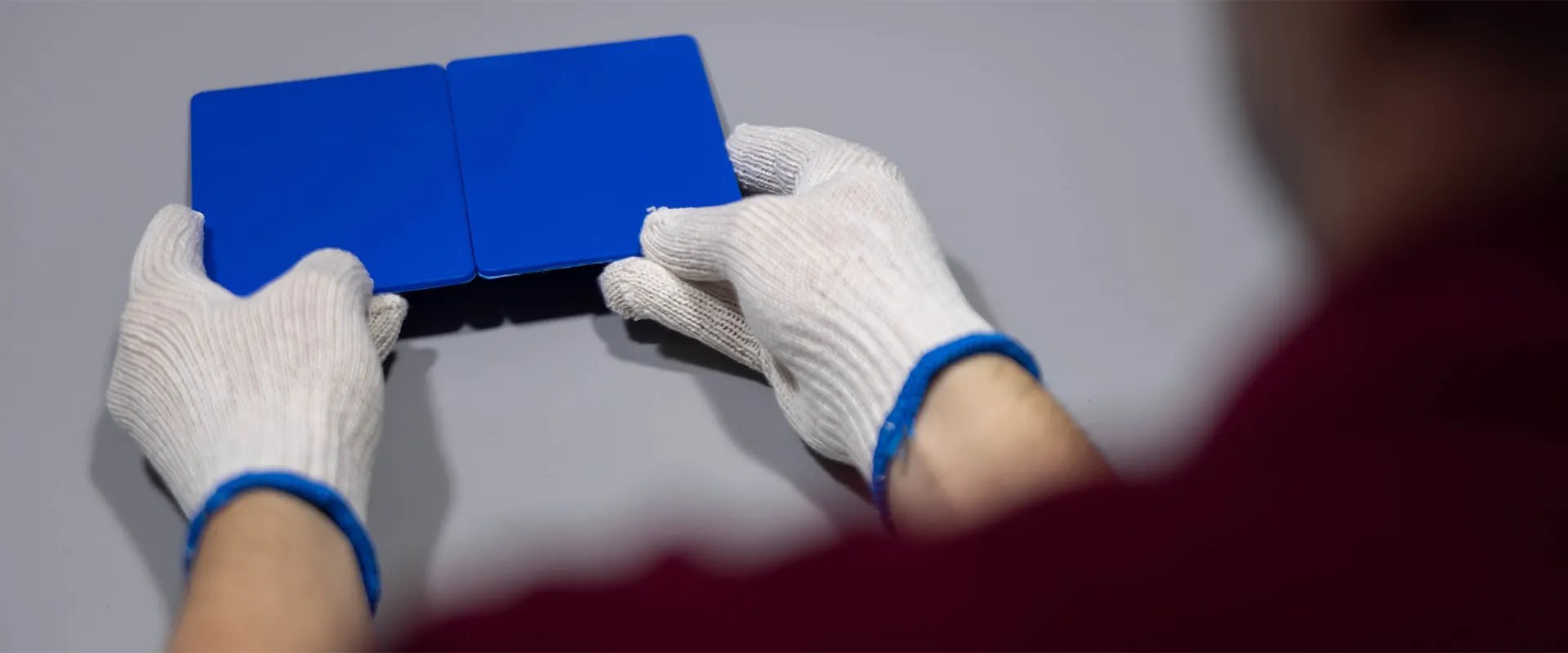 A person wearing white gloves is holding and aligning two blue rectangular panels on a gray surface.