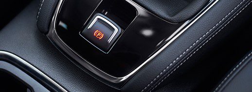 Close-up of a car's electronic parking brake button with an illuminated red indicator light, surrounded by black leather and chrome trim.