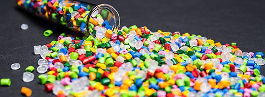 A glass container spills multicolored plastic pellets onto a dark surface.