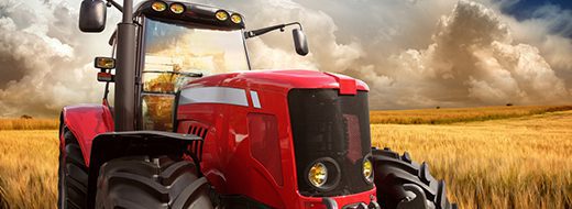 A red tractor is parked in a golden wheat field under a cloudy sky.
