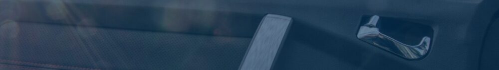 Close-up of a car door interior showing a silver door handle and part of the seatbelt.