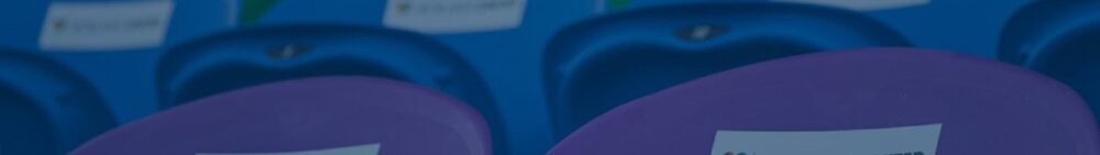 Rows of empty blue and purple stadium seats, each with a paper notice attached to the backrests.