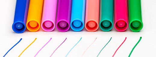 Eight colored markers are arranged in a row, each with a matching line of ink drawn beneath them on a white surface.