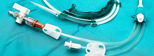 Medical catheters and tubes on a teal surgical drape, arranged with connectors and clamps visible, used for fluid delivery or drainage in clinical settings.