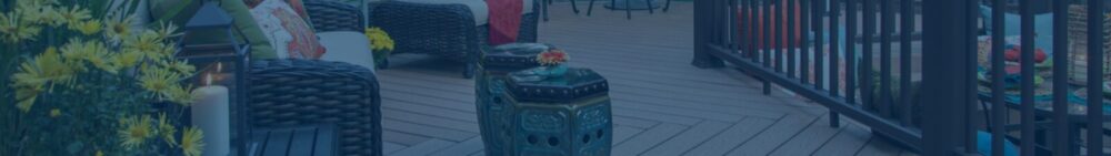Wicker patio furniture and a ceramic side table are arranged on a wooden deck, with potted yellow flowers visible on the left side.