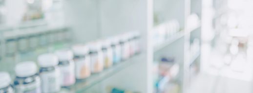 Blurred image of shelves lined with various pill bottles and containers in a pharmacy or medical supply store.