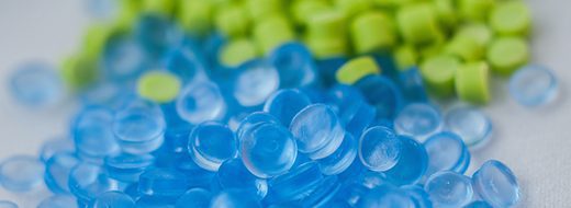 Close-up of translucent blue plastic pellets and opaque light green pellets scattered on a white surface.