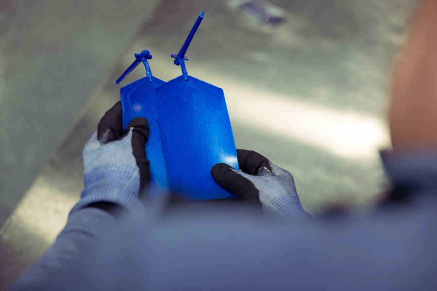 A person wearing gloves holds a blue plastic object with two protruding antennas or rods, viewed from above.