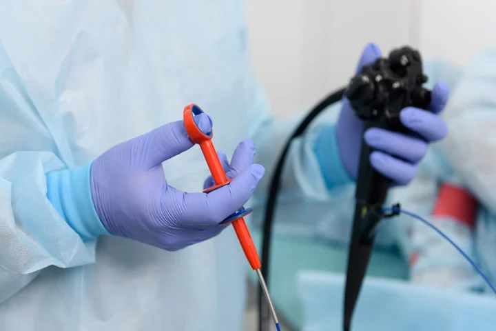 A medical professional wearing gloves holds an endoscope and a surgical instrument in a clinical setting.