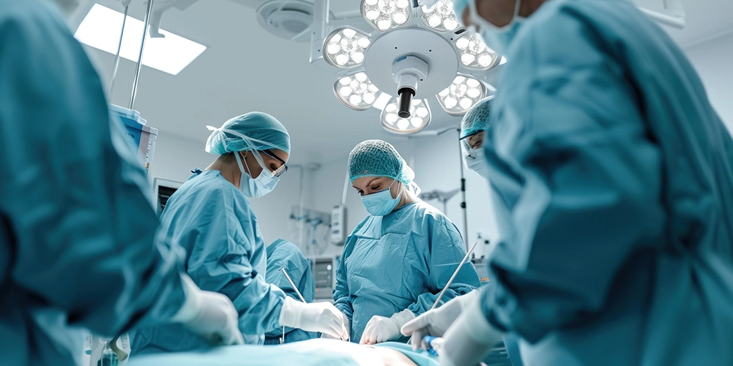 Several surgeons in blue scrubs and masks perform an operation in a brightly lit hospital operating room.