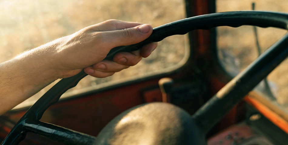 A close-up of a person's hand gripping a steering wheel inside a vehicle, with sunlight coming through the window.