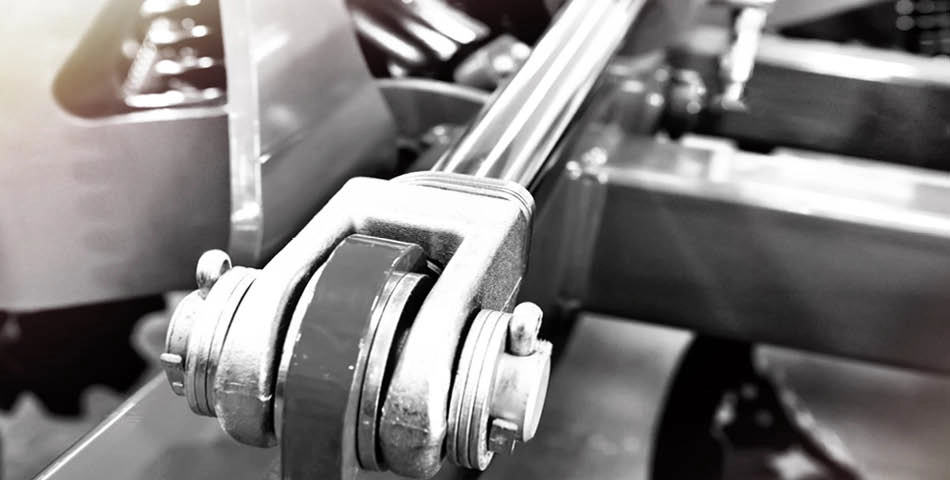 Close-up view of a metal hydraulic piston mechanism in industrial machinery, showing bolts, joints, and connecting rods in a monochrome setting.