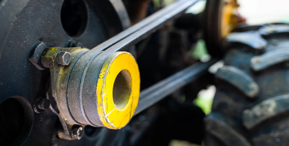 Close-up of a yellow pulley wheel with a belt connected to machinery, next to a large black rubber tire.