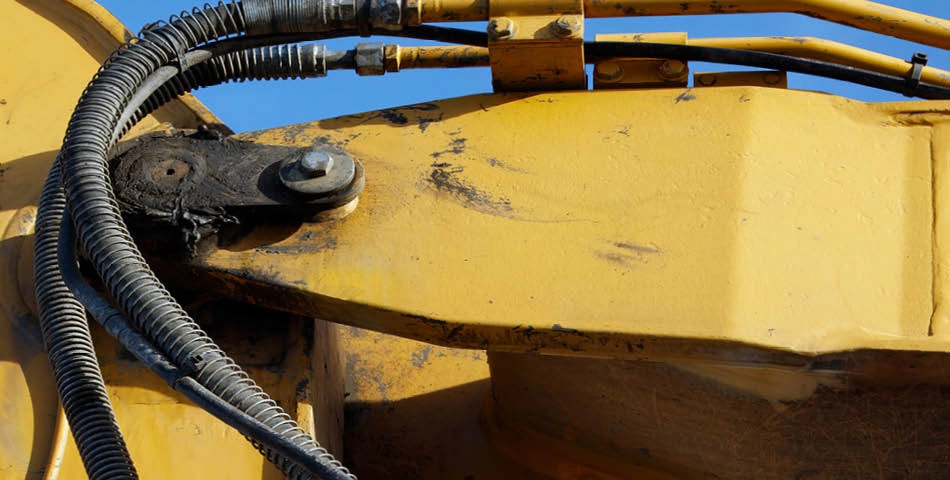Close-up of a yellow construction vehicle arm showing hydraulic hoses, bolts, and visible wear marks.