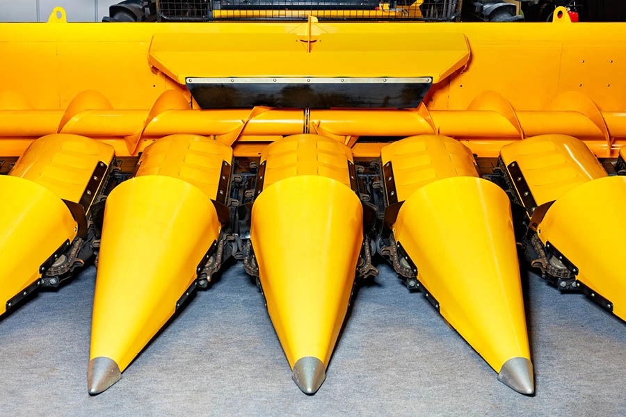 Close-up view of the front end of a yellow combine harvester head, showing several pointed cones aligned side by side.