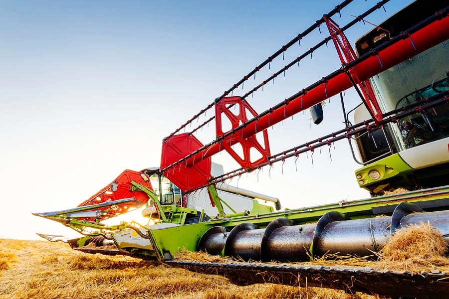 Close-up of a modern combine harvester cutting and gathering crops in a field under a clear sky.