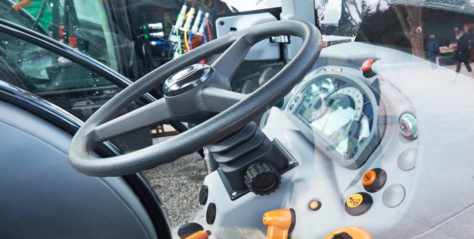 Close-up view of a modern tractor dashboard with a steering wheel, various control levers, buttons, and digital display gauges.
