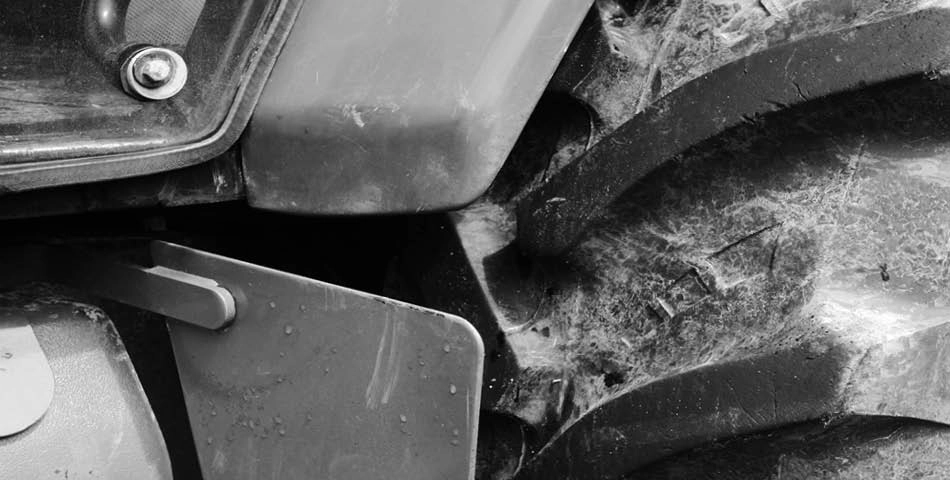 Close-up black and white view of a large, dirty tractor tire and part of the tractor’s chassis.